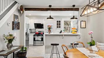 A kitchen with white cabinets, a central island, pendant lighting, and a dining area with a wooden table and chairs.