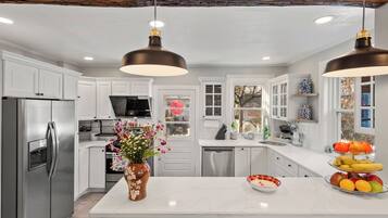 A modern kitchen with white cabinets, stainless steel appliances, a marble island, and pendant lighting.