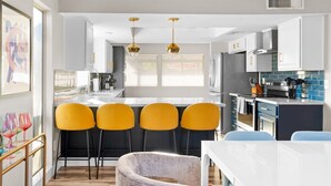 Una cocina moderna con una isla central, taburetes amarillos y una mesa de comedor blanca.