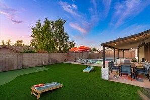 A backyard with artificial grass, a pool, a table with chairs, and a covered seating area. - Backyard Game Day HQ | Pool, Hoops & Putt Putt (Glendale)