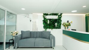 Ein Empfangsbereich mit grauem Sofa, weißem Empfangstresen und einer grünen Wand mit vertikalem Garten.