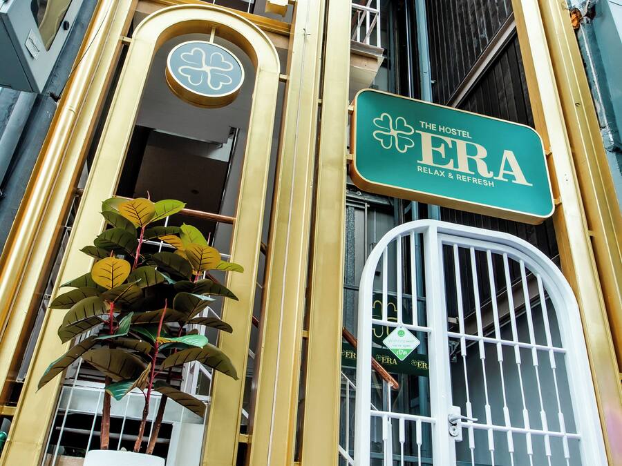 Un hostal con un letrero verde y blanco, una planta grande en maceta y una puerta blanca con reja de metal.