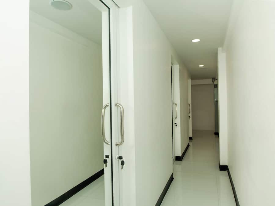 Un pasillo limpio y moderno con paredes blancas y detalles en negro, que conduce a una puerta con manija y cerradura.
