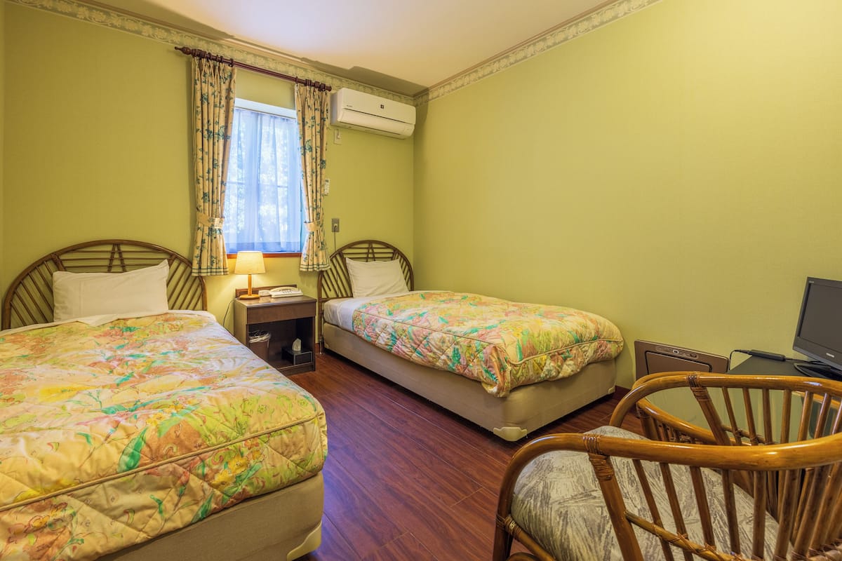A room with two beds, a chair, a desk, and an air conditioning unit.