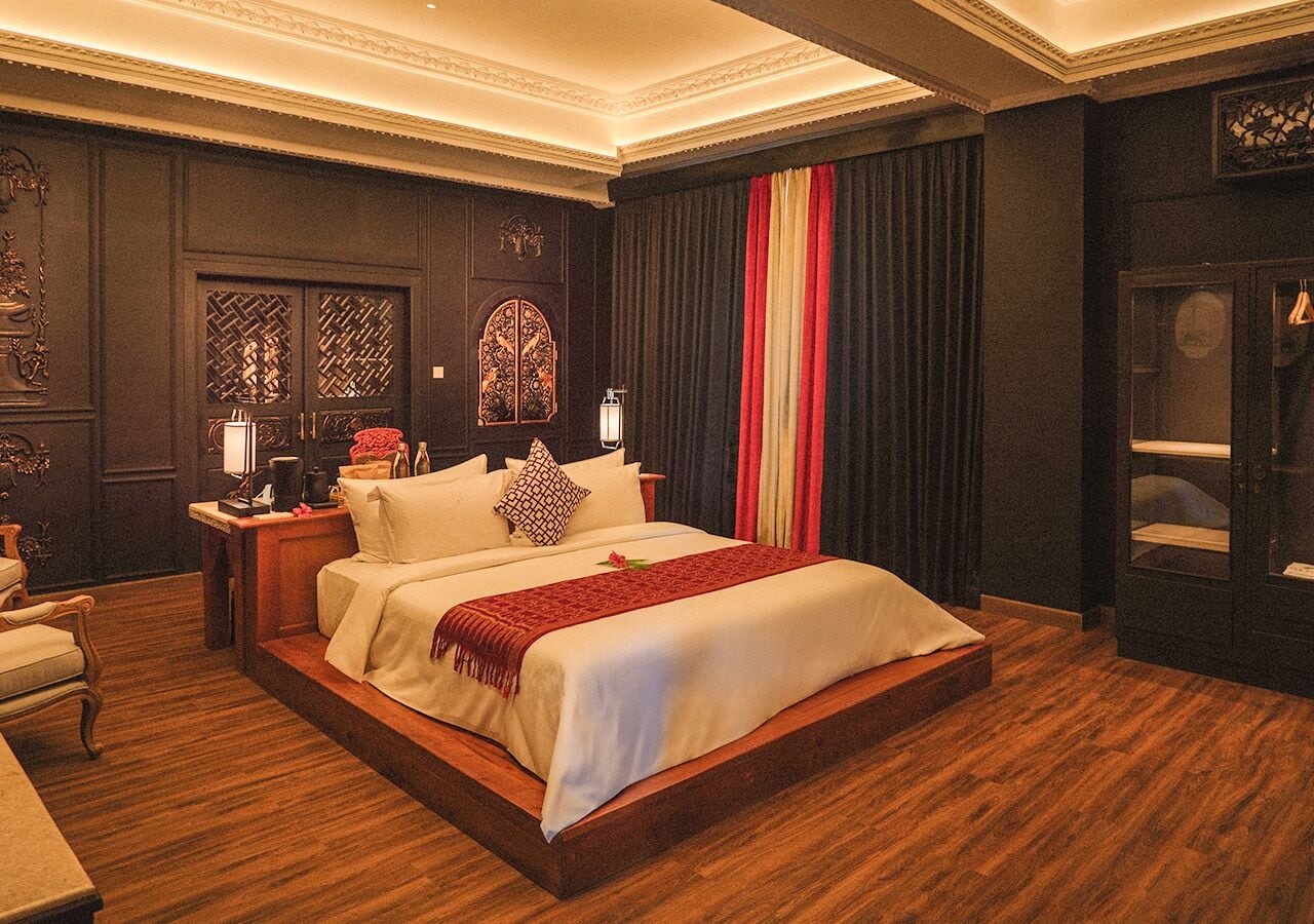 A spacious bedroom with a large bed, wooden flooring, and dark walls with decorative panels.