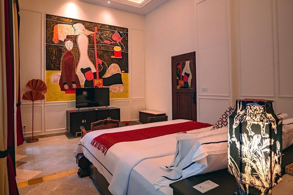 A hotel room with a large abstract painting on the wall, a bed with a red blanket, a television, and a decorative vase.