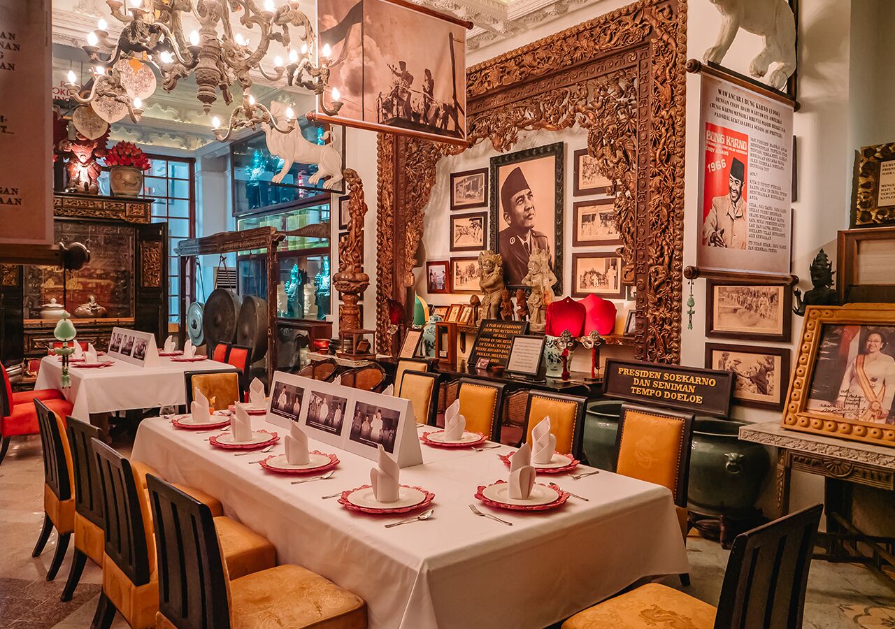 A restaurant with tables set for dining, featuring ornate wall decorations and framed pictures.