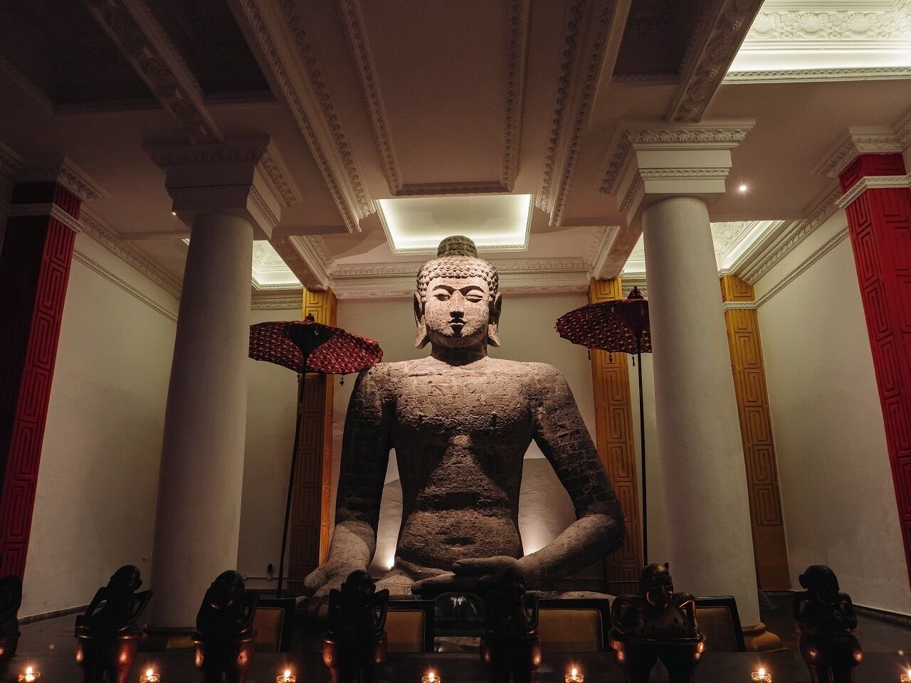 A large Buddha statue in a room with columns and chandeliers.