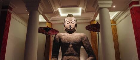A large Buddha statue in a room with columns and chandeliers.