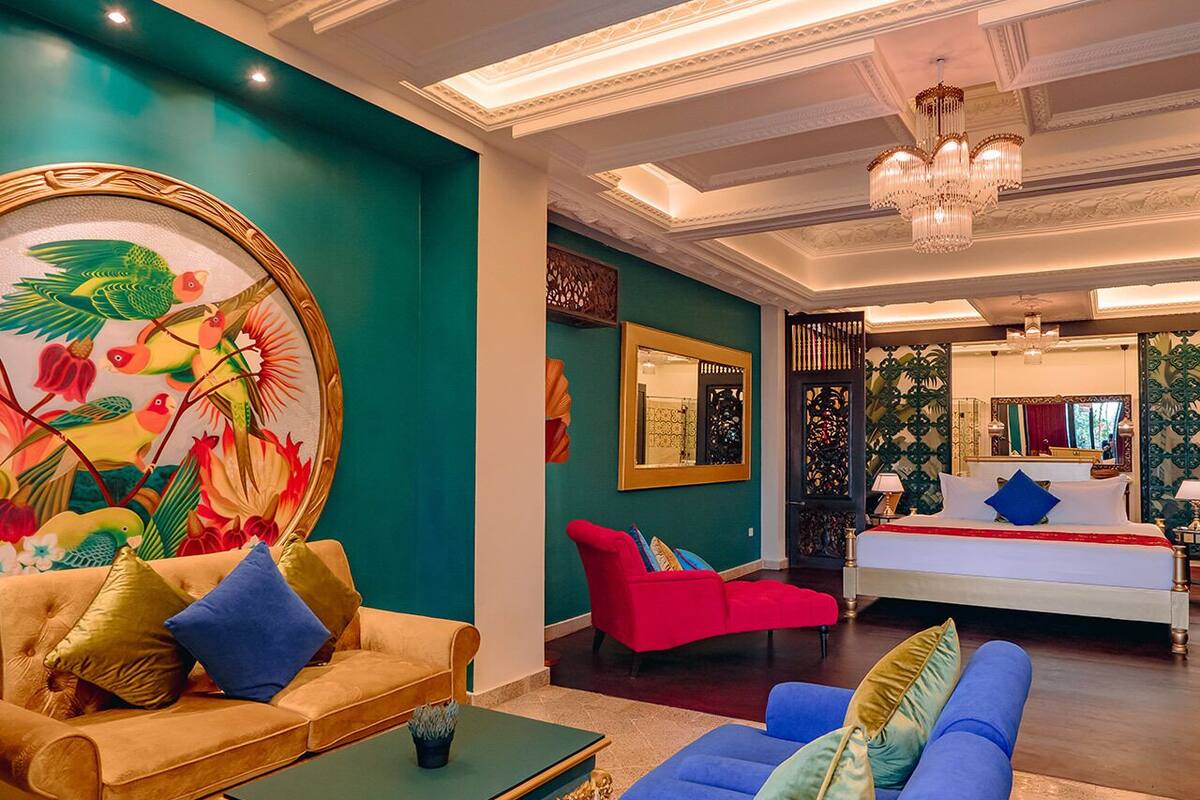 A hotel room with a large bed, a red armchair, a blue sofa, and a colorful mural on the wall.