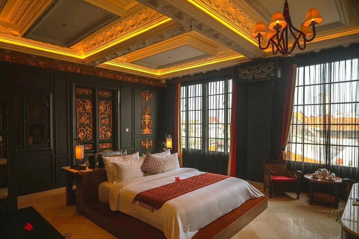 A large bed with a red throw, a nightstand, a chair, and a table with a lamp.