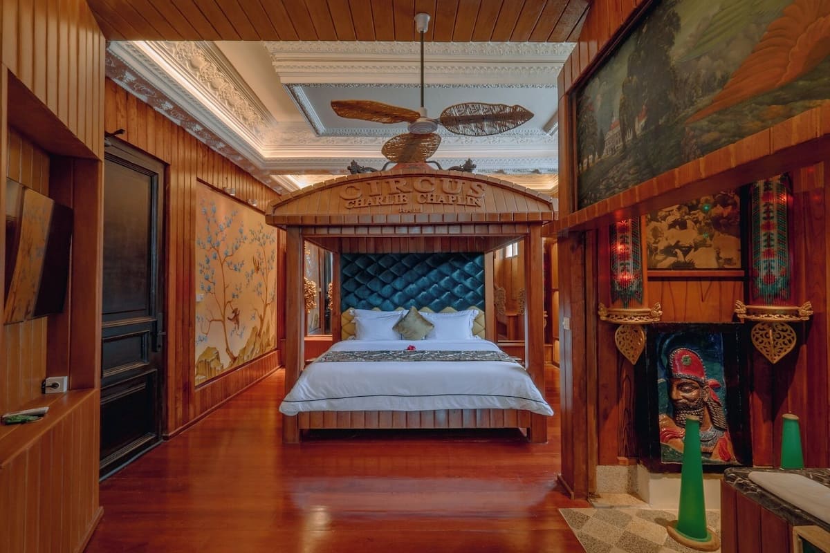 A luxurious bedroom with a large bed, wooden paneling, a decorative ceiling fan, and a fireplace.