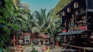 An outdoor seating area with tables and chairs, surrounded by lush greenery and palm trees. - House of Tugu Old Town Jakarta (Jakarta)