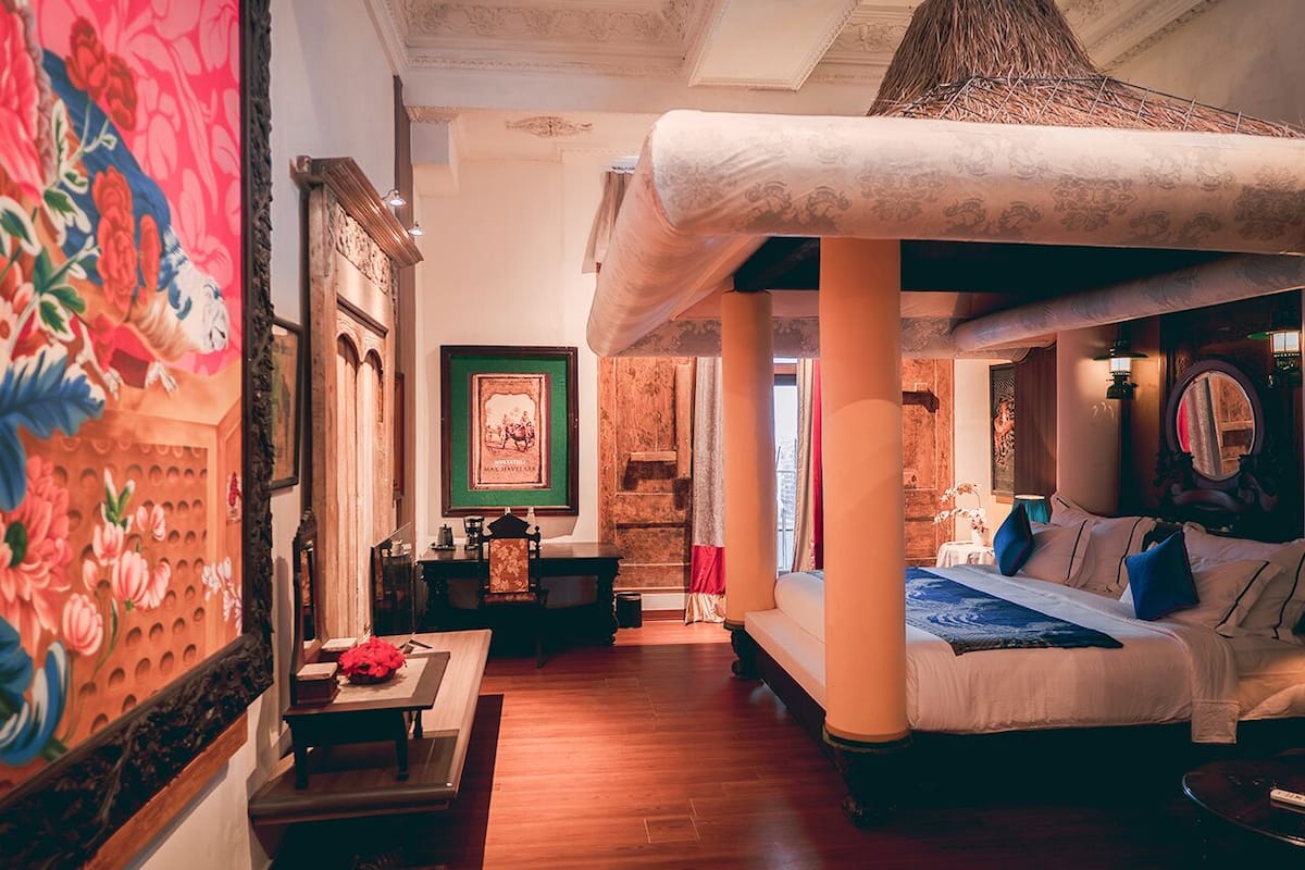 A hotel room with a large bed, a sitting area with a table and chairs, a fireplace, and a large painting on the wall.