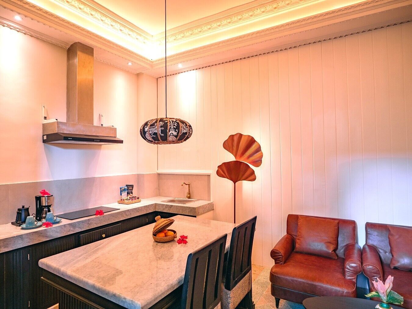 A modern kitchen with a dining area, featuring a marble countertop, a built-in oven, and a hanging light fixture.