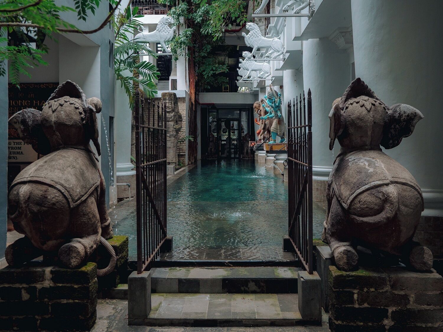 A courtyard with a central water feature, flanked by elephant statues and a staircase leading to an upper level.