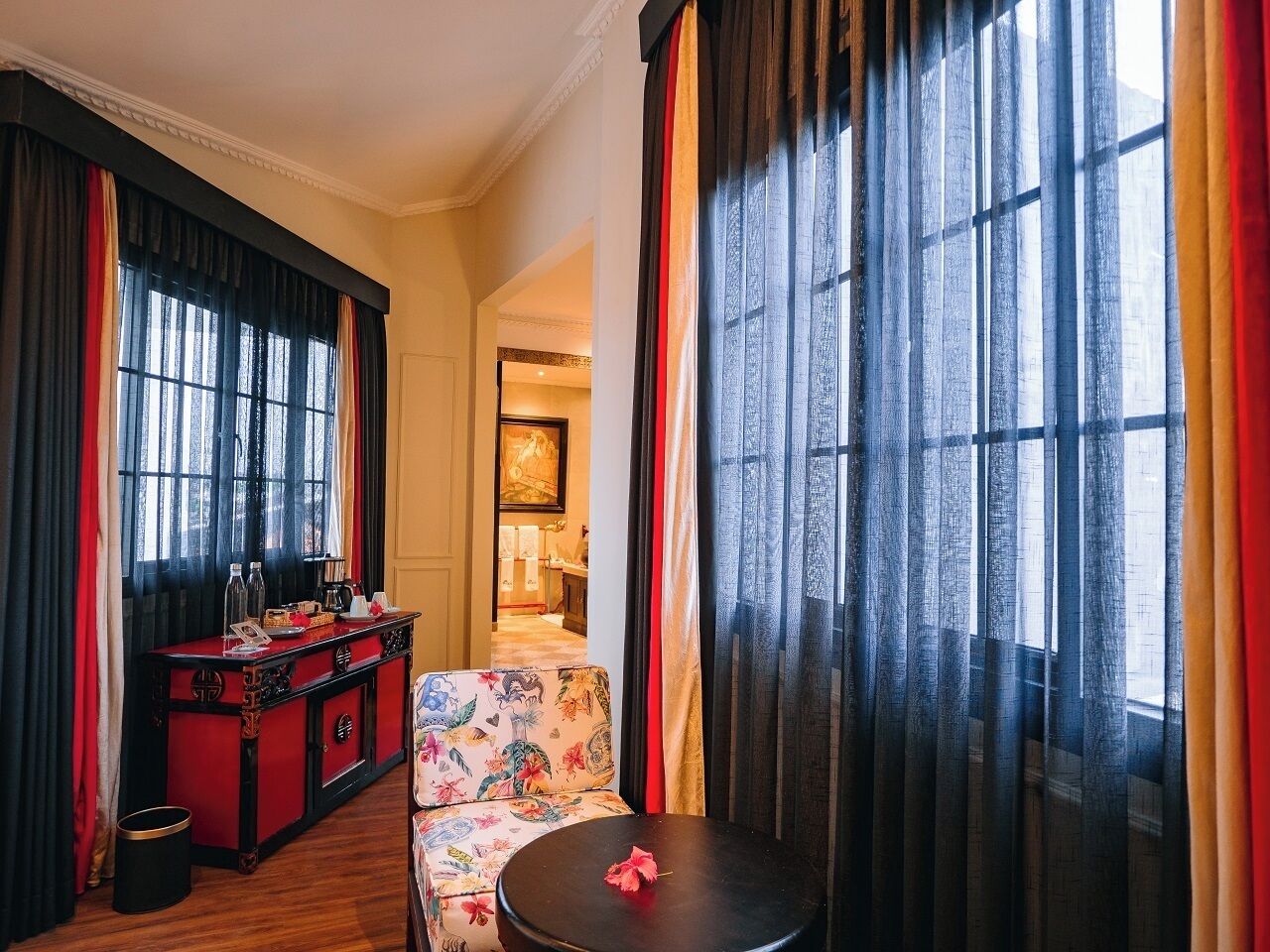 A room with a red and black minibar, a floral sofa, and a small round table with a red flower.