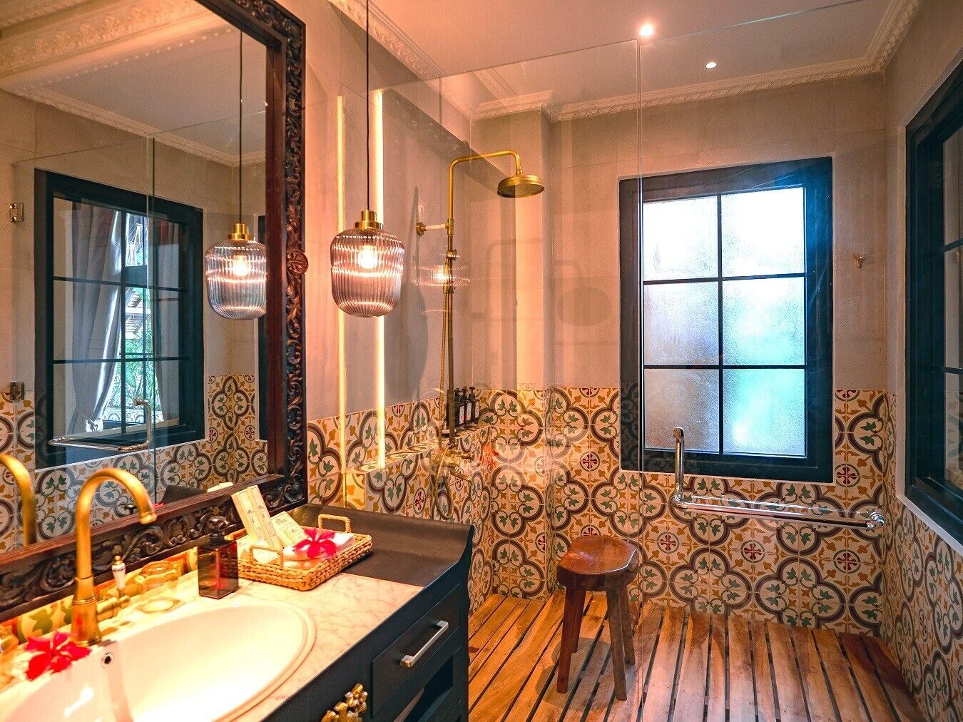 A bathroom with a large mirror, a bathtub, a window, and patterned tiles.