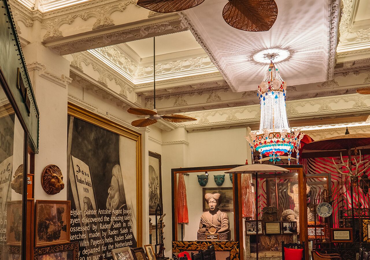 A room with ornate ceiling details, a chandelier, and various framed artworks.