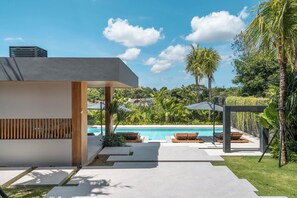 A modern outdoor pool area with lounge chairs, a pergola, and a view of a residential neighborhood. - Beyond The Palms (Canggu)