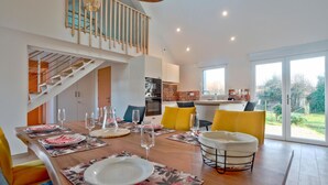 A modern dining area with a wooden table set for four, a staircase, and a kitchen in the background. - Awesome home in Flottemanville-hague with WiFi (Flottemanville-hague)