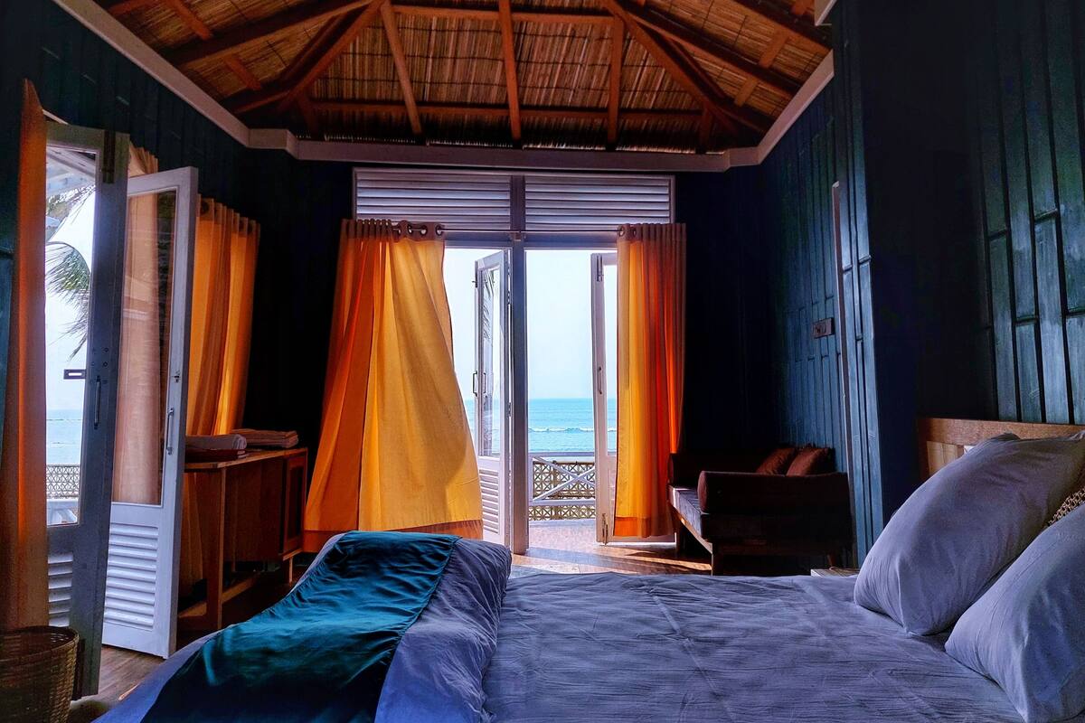 Une chambre avec un lit, une chaise, un bureau et une vue sur l’océan, visible à travers une porte vitrée.