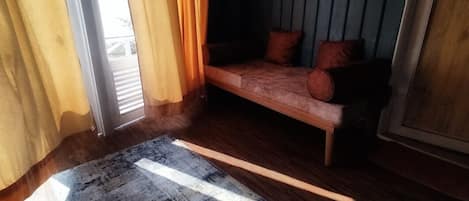 A room with a wooden floor, a sofa with cushions, and a window with curtains.