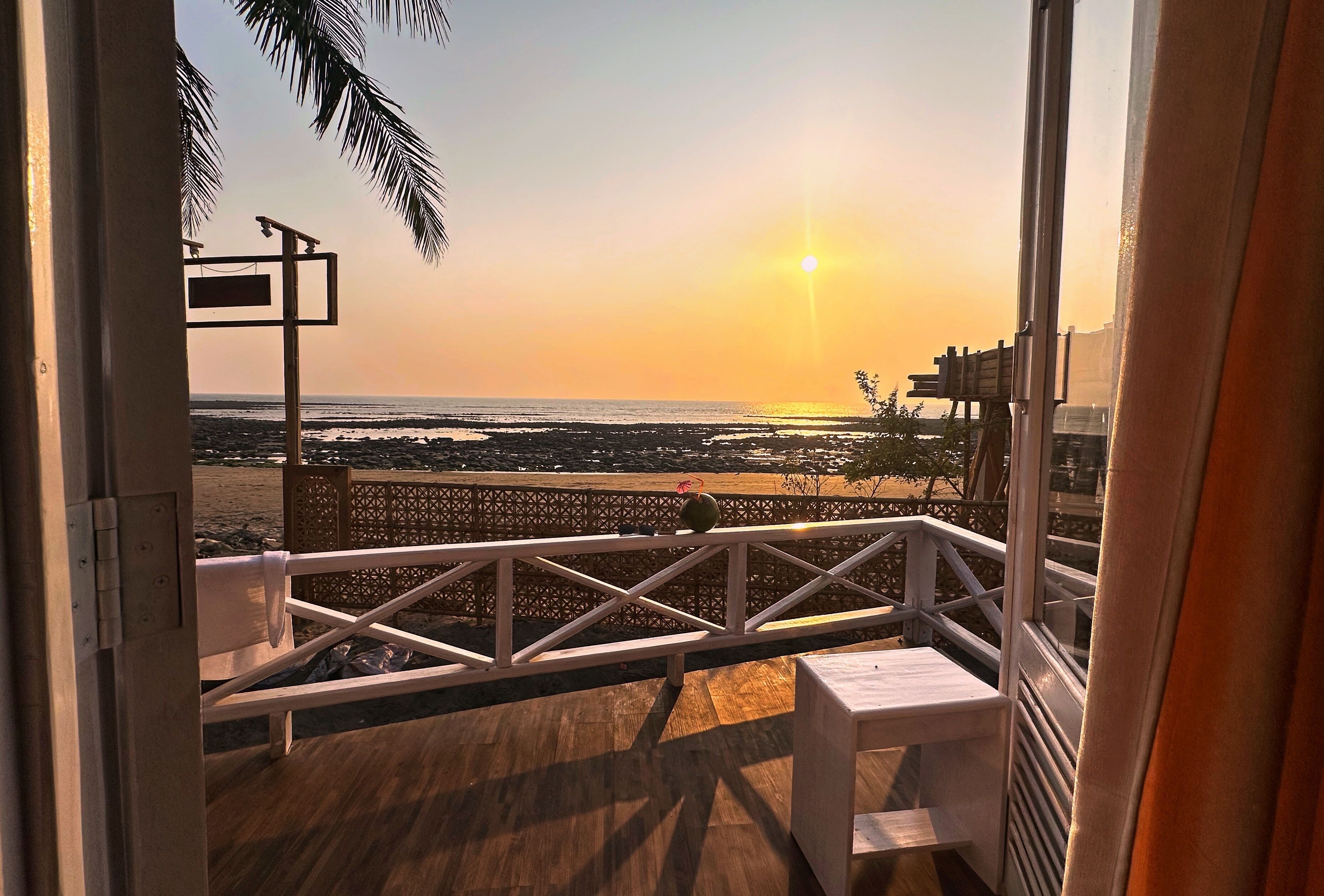 A balcony with a view of the beach and ocean at sunset.