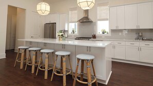 A modern kitchen with white cabinetry, a central island with stools, stainless steel appliances, and pendant lighting. - Magnolia Manor by Apex Short Term Stays (Oxford)