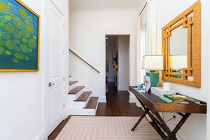Un couloir avec un escalier en bois, un miroir et un tableau encadré.