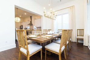 A dining area with a wooden table and chairs, a chandelier, and a view into the kitchen.