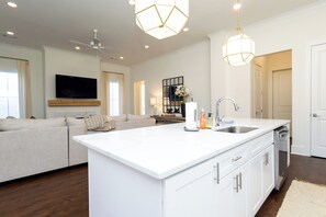 A modern living room with a large white sofa, a flat-screen TV mounted on the wall, and a ceiling fan.
