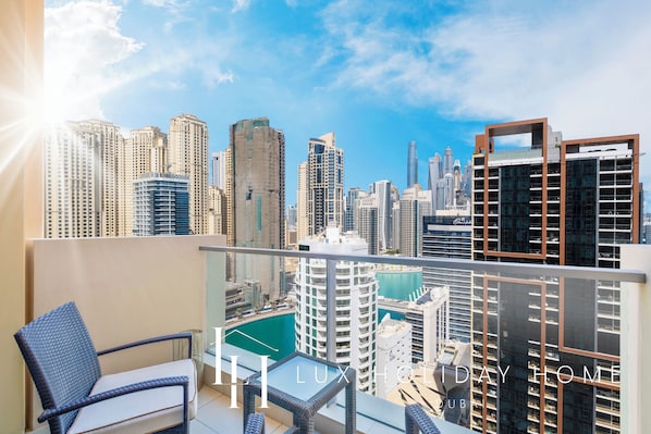 A balcony with a city view, wicker furniture, and a glass table.