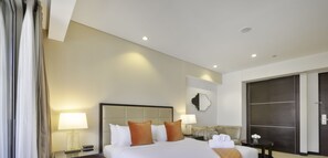A hotel room with a large bed, two bedside tables with lamps, a sofa, and a dark wooden wardrobe.