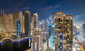 A nighttime cityscape with high-rise buildings, a waterfront, and illuminated signage.