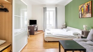 Une chambre d’hôtel avec un lit, un bureau avec un ordinateur, une télévision, un canapé et un tableau au mur.