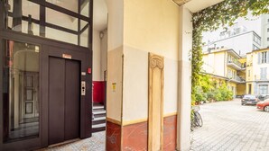 Une entrée d’immeuble avec une porte sombre, un mur rouge et un sol carrelé.