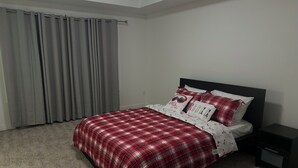 A bedroom with a bed, grey curtains, and a nightstand. - Spacious 3-Bedroom Apartment in  – Perfect for Groups & Families! (Calgary)