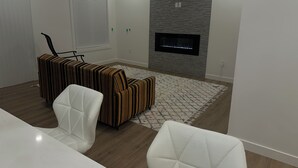 A modern living room with a fireplace, striped sofa, and white chairs. - Spacious 3-Bedroom Apartment in  – Perfect for Groups & Families! (Calgary)