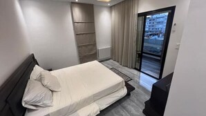 Un dormitorio moderno con una cama, un estante empotrado, una puerta corrediza de vidrio a un balcón y vistas de la ciudad.