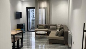 Una sala de estar moderna con un sofá seccional, una mesita redonda y un televisor montado en la pared.