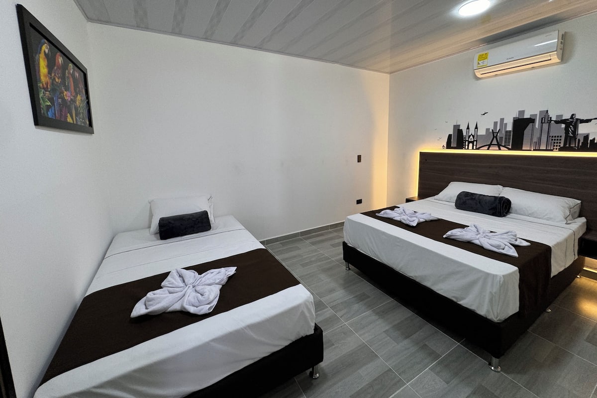 A hotel room with two beds, a cityscape mural on the wall, and an air conditioning unit.