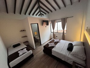 A hotel room with two single beds, a bathroom with a toilet and sink, a mirror, and a window with curtains. - Hotel Paraiso Cañaveral (Santa Fe de Antioquia)