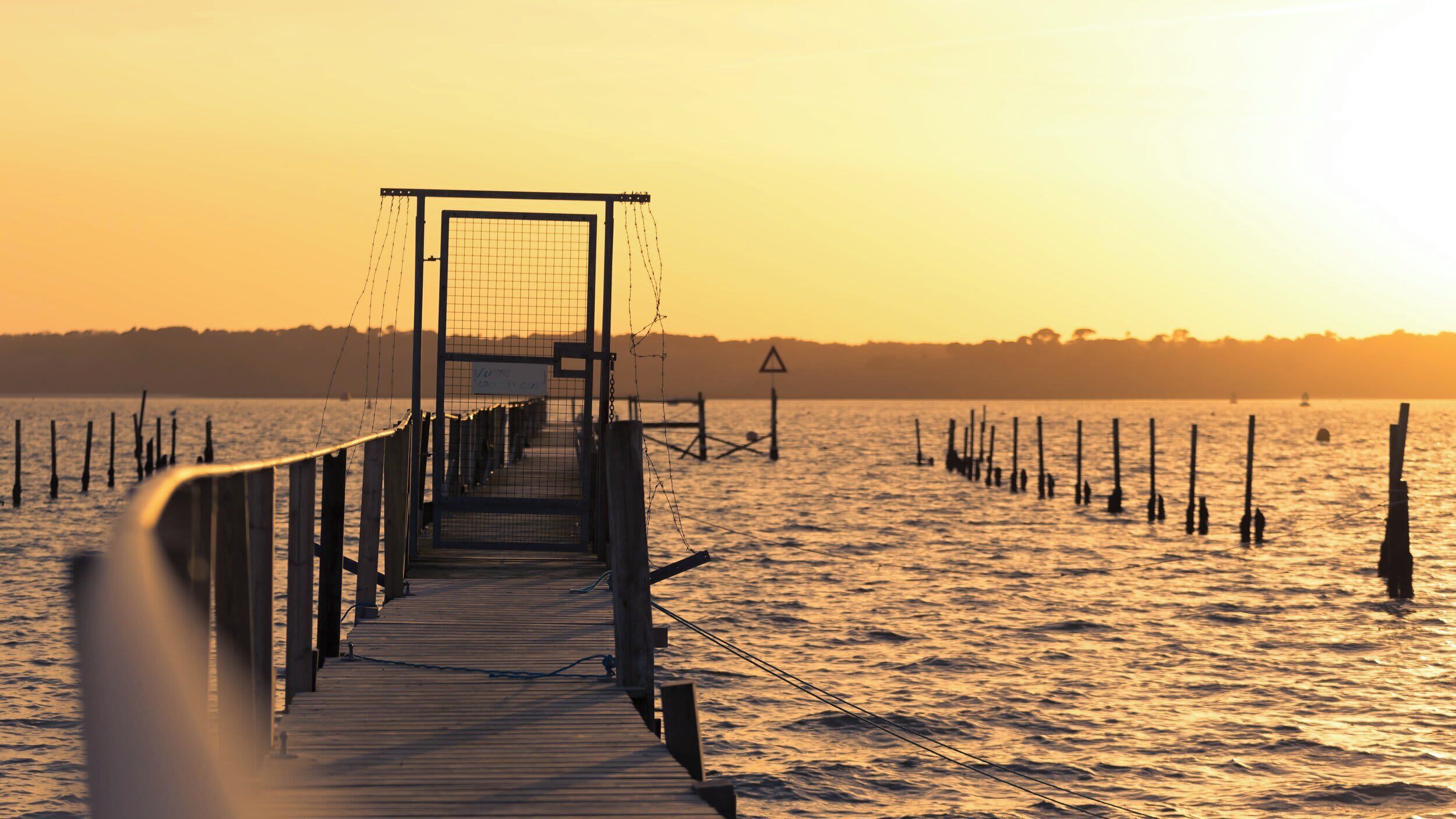 A wooden pier extending into calm water with a sunset in the background.