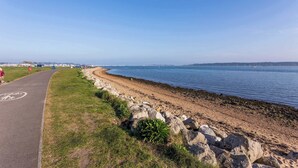 A coastal road with a paved path, rocky shoreline, and a clear view of the sea.