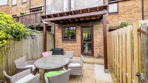 A patio with wicker furniture, a glass table, and a wooden fence.