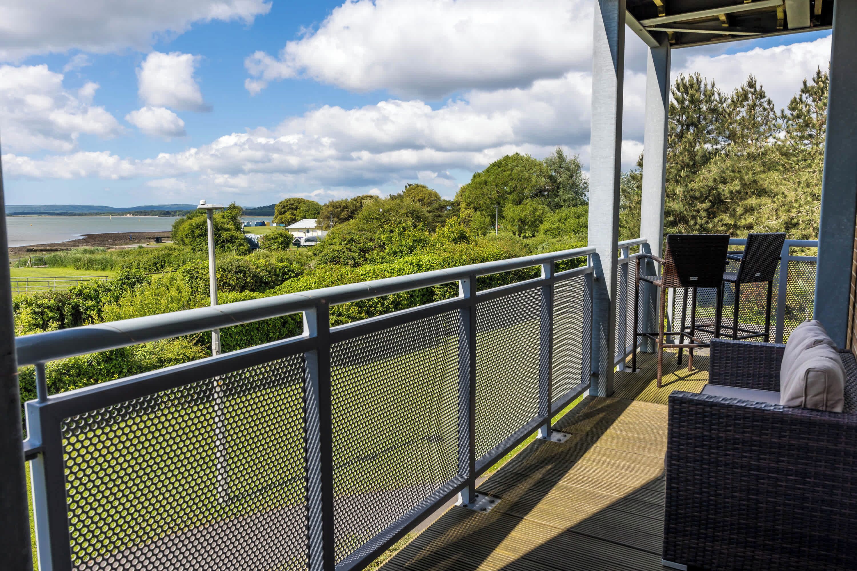 Ein Balkon mit Seeblick, umgeben von viel Grün und mit Korbmöbeln.