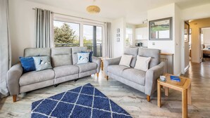 A modern living room with two grey sofas, a blue rug, and a wooden coffee table.