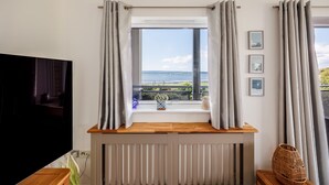 A room with a large window, a wooden console table, a radiator, and a television.