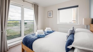 A bedroom with a large bed, two windows, a view of greenery, and a ceiling light.